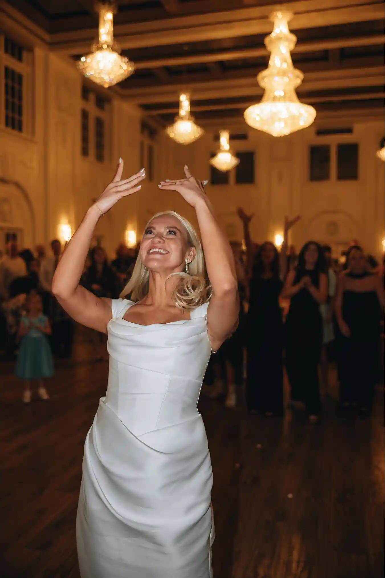 Wedding party cheering with the couple in a bright ballroom aisle
