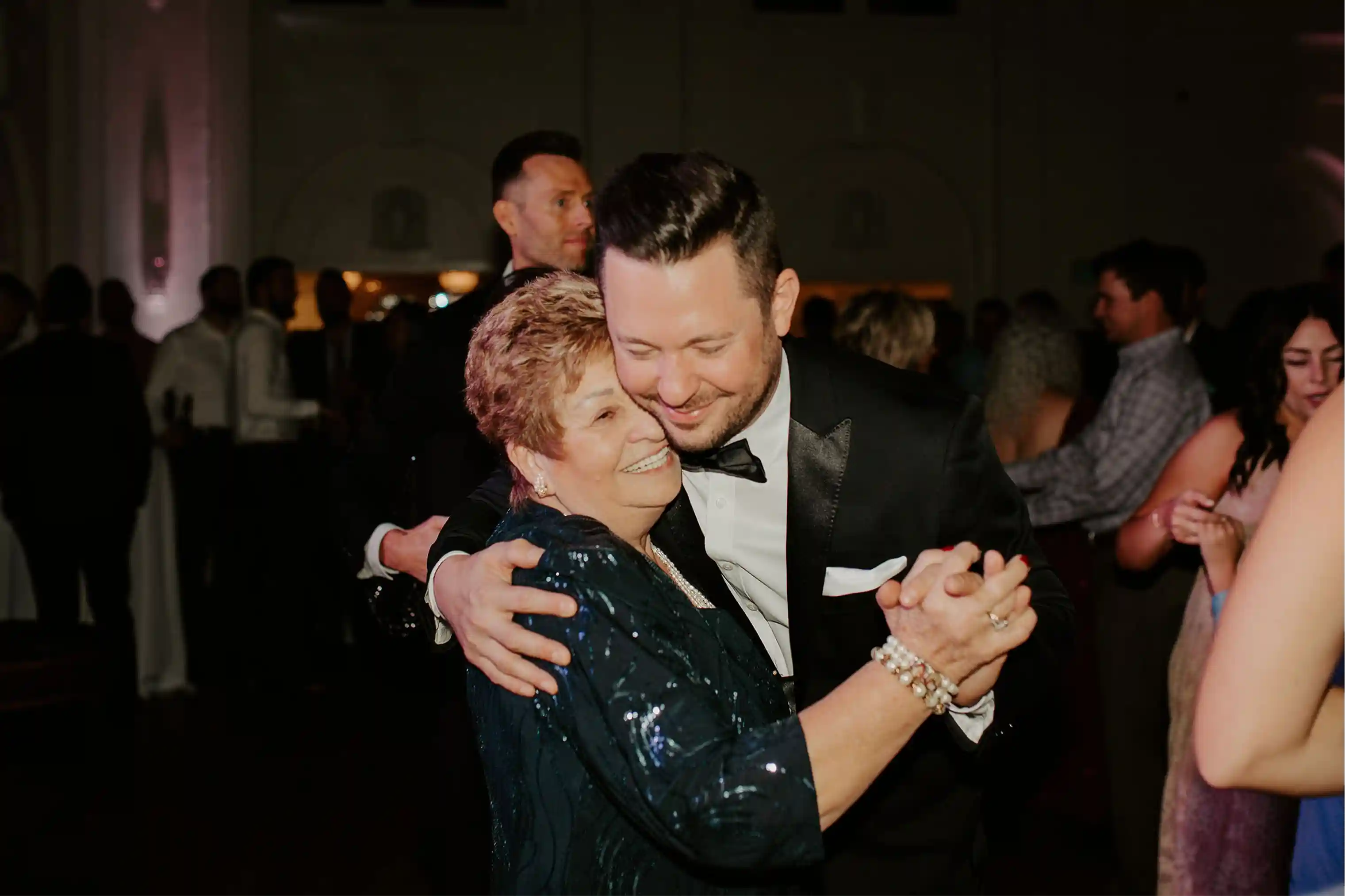 Couple kissing while white petals fall inside the ballroom